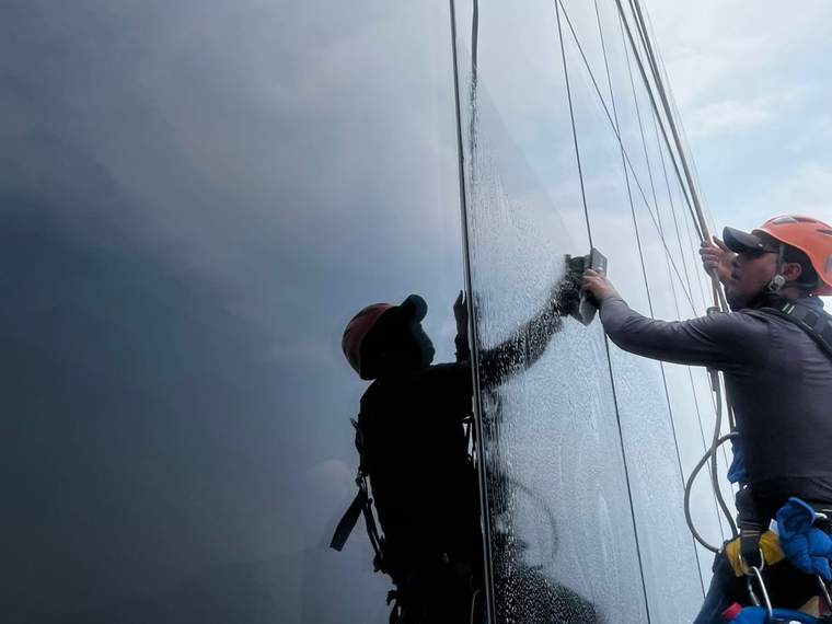 Técnico enjuagando cristal de fachada con goma de limpieza